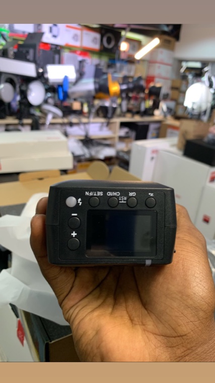 A Godox trigger held in the shop, lighting stock behind